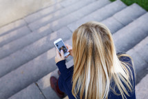 woman sitting on steps looking at her cellphone 