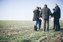 group of people holding hands in prayer in a field