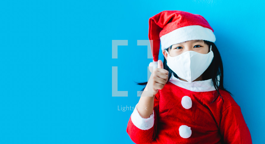a little girl in a Santa Suit wearing a face mask 