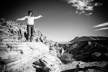 woman standing with her arms out on a cliff over looking mountains 