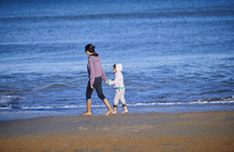 bare mother and daughter walking on a beach 