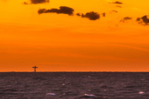 Sunset over the ocean with a cross in the distance.
