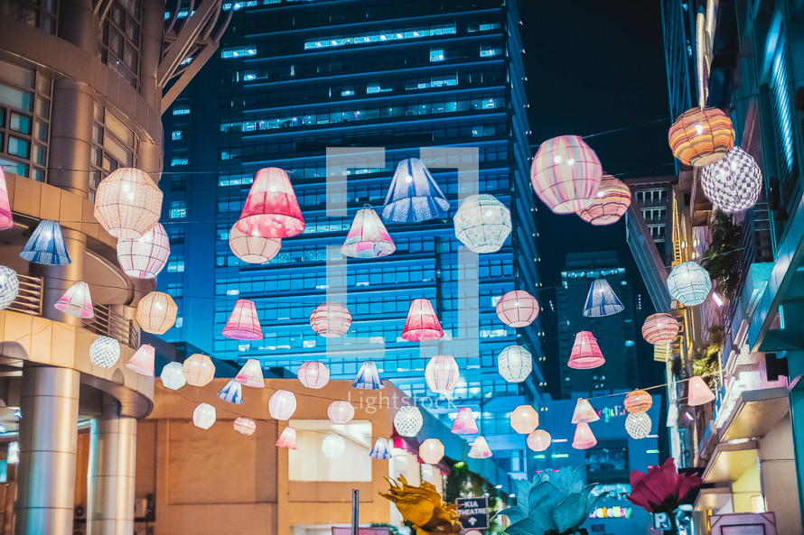 paper lanterns hanging between buildings in a city at night 