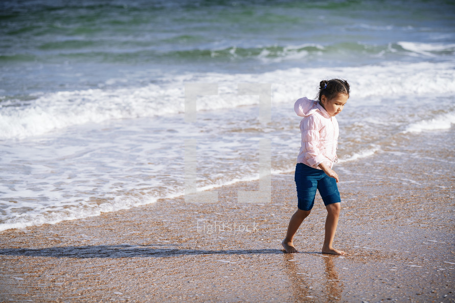 child walking on a beach in a coat 
