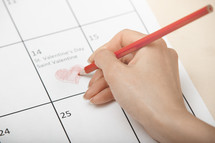 Woman hand drawing heart on a calendar at Valentine Day