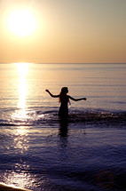 a young woman walking into water at sunset 