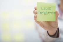 a woman holding a sticky note with the words under construction 