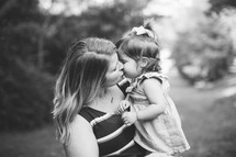 a mother kissing her toddler daughter in black and white 