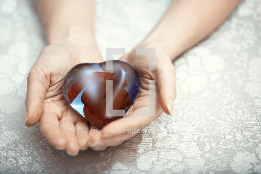 cupped hands holding a glass heart 