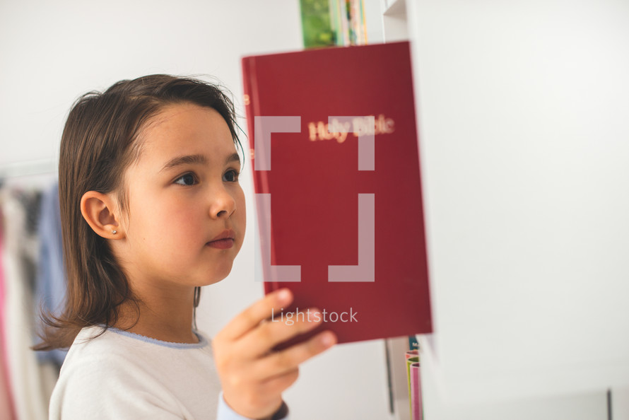 a child taking a Bible off a bookshelf in a library 