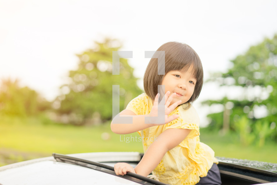 toddler girl waving out of a sunroof 