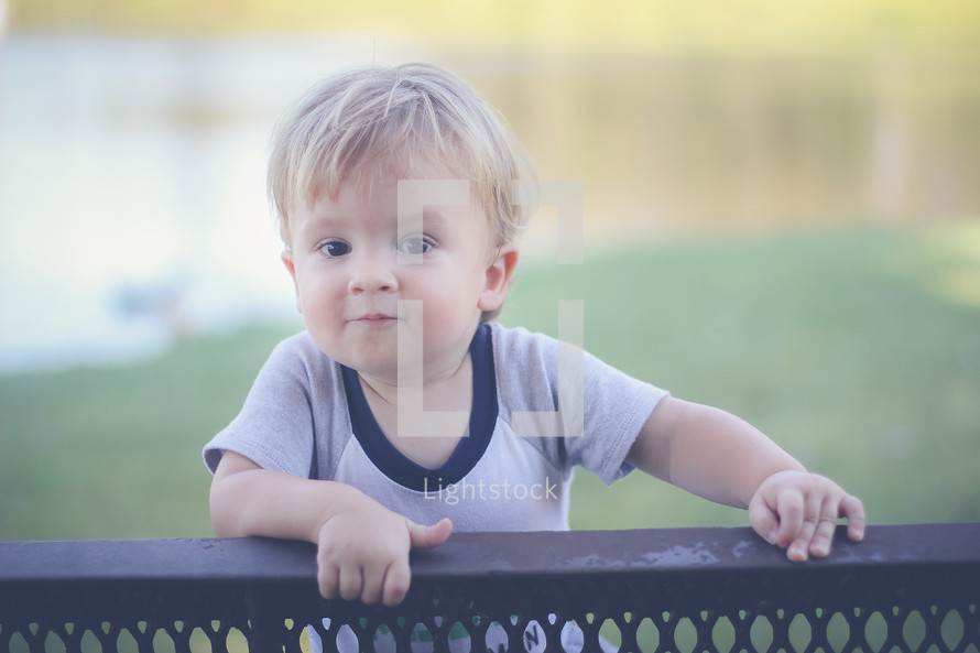 a toddler boy looking over the back of a park bench 