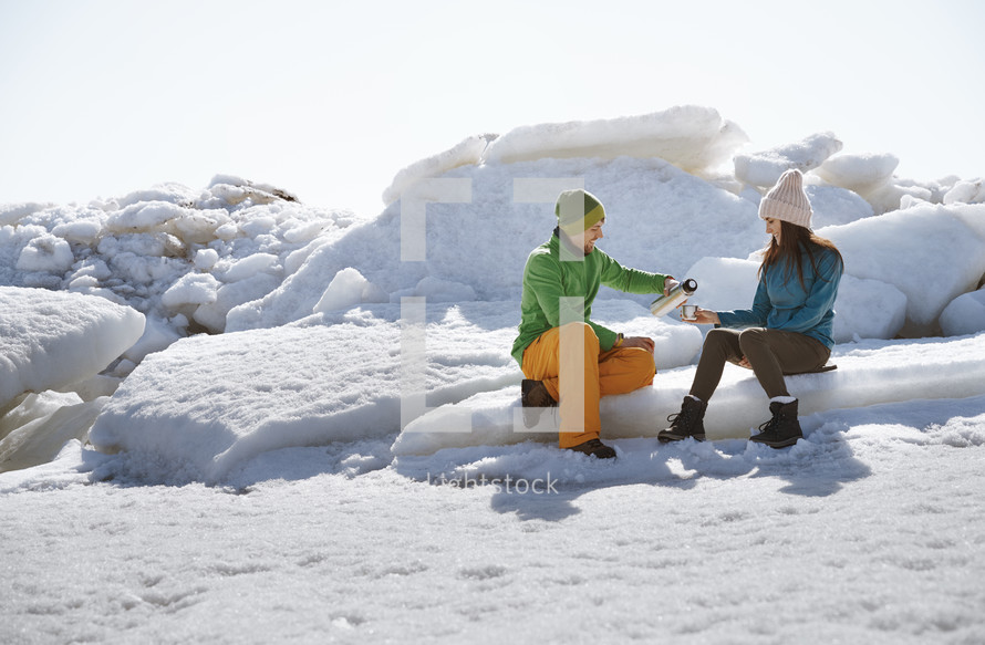 couple pouring coffee from a thermos in snow 