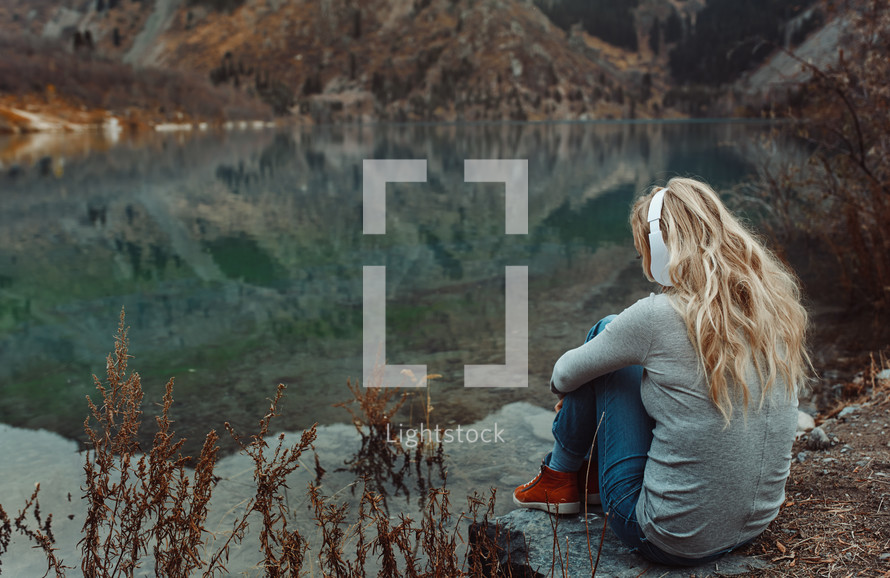 a woman listening to headphones by a lake 