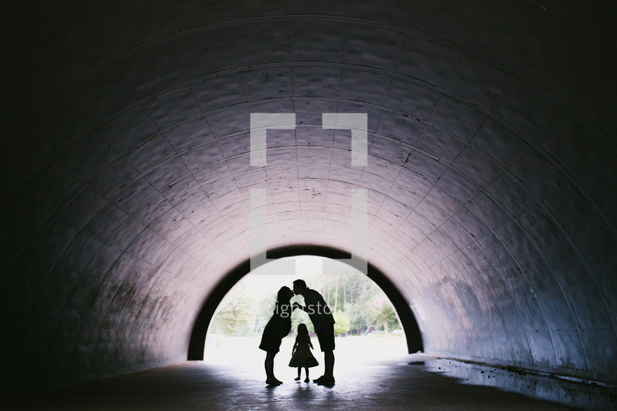 silhouettes of a mother and father kissing in a tunnel and a child standing between them 