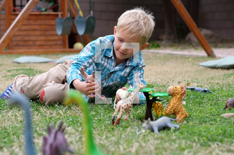 a kid playing with toy animal figurines in grass