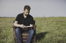 A man sitting in a leather chair reading a Bible 
