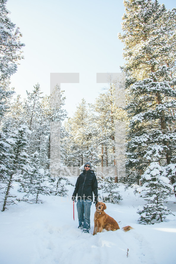 man walking through a snowy forest with his dog 