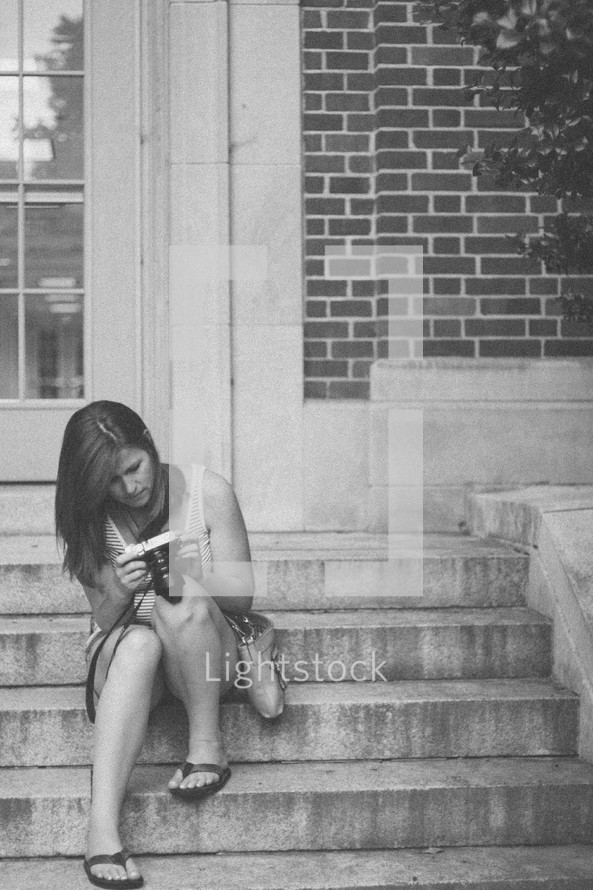 woman sitting on steps looking at her camera 