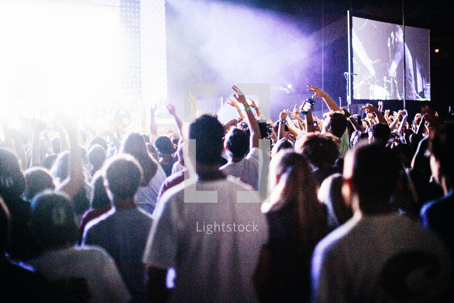 raised hands under spotlights at a concert 
