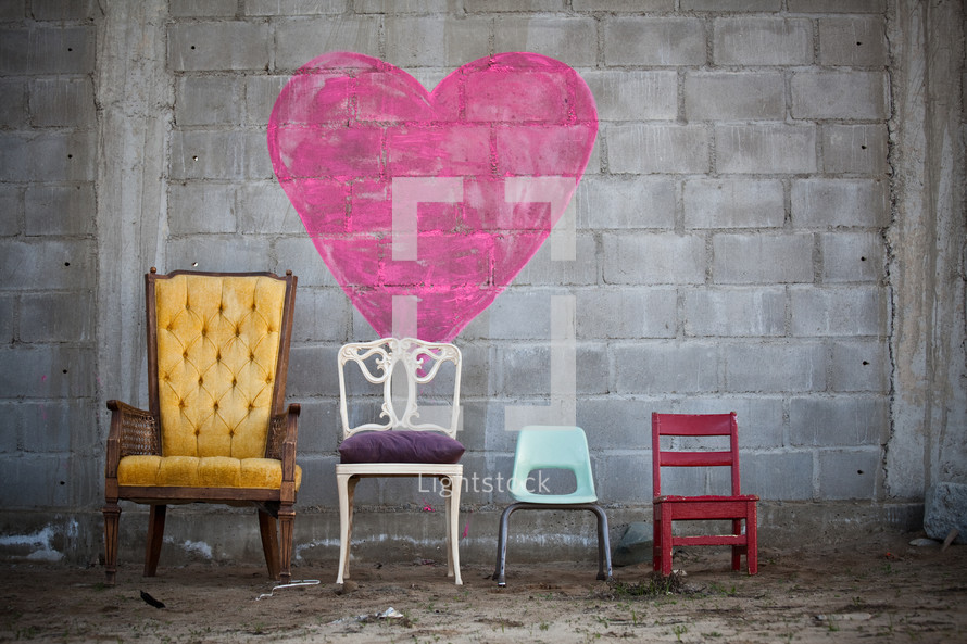 Family chairs in the dirt by a heart painted on a brick wall.