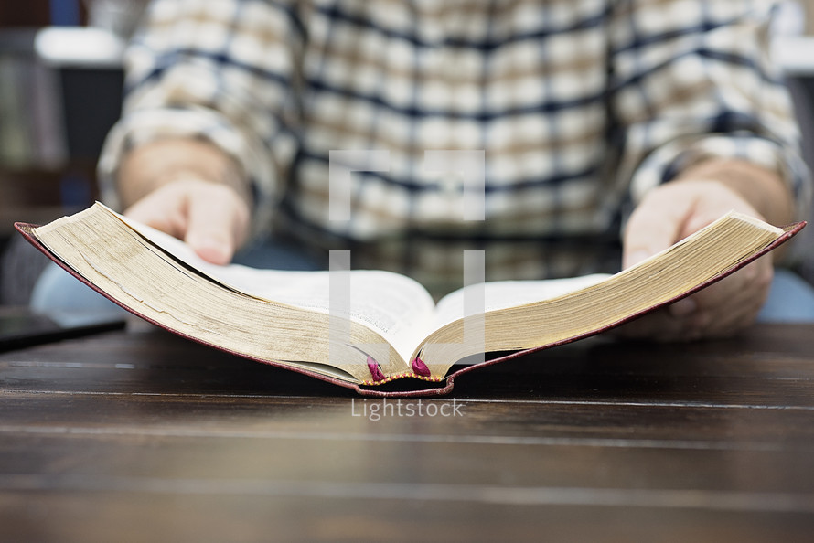 a man in a plaid shirt reading a Bible on a coffee table 