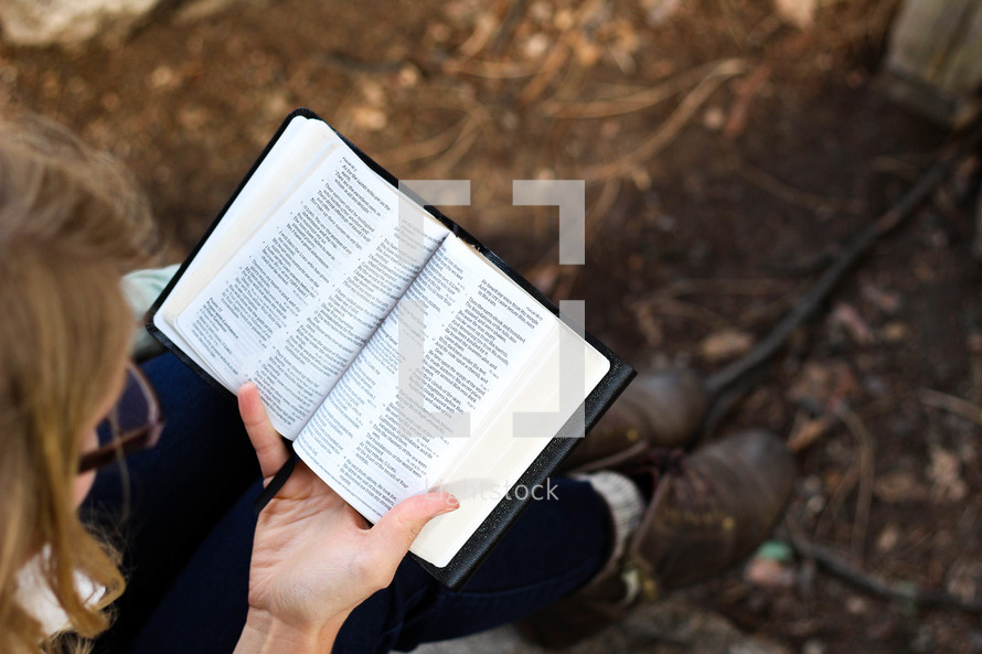 A woman sits and reads her Bible outdoors.