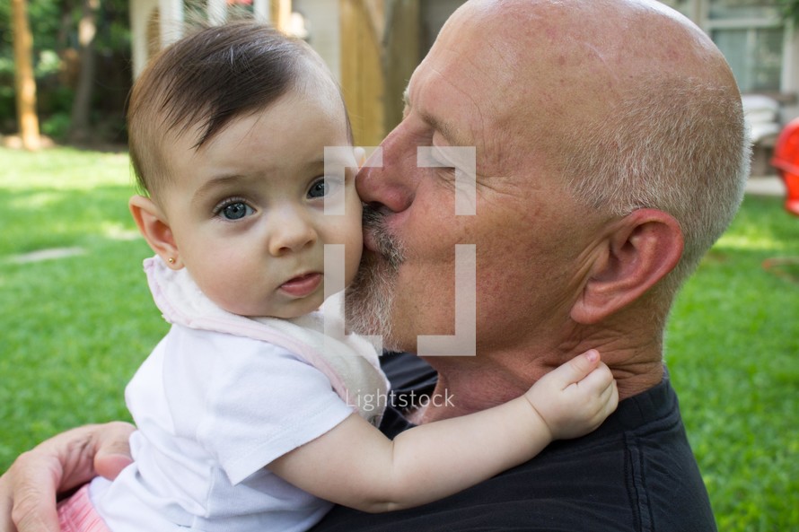 a grandfather kissing his baby granddaughter 