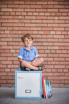 a boy sitting on a locker next to books 