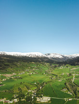 aerial view over a green valley surrounded by snow capped mountains 