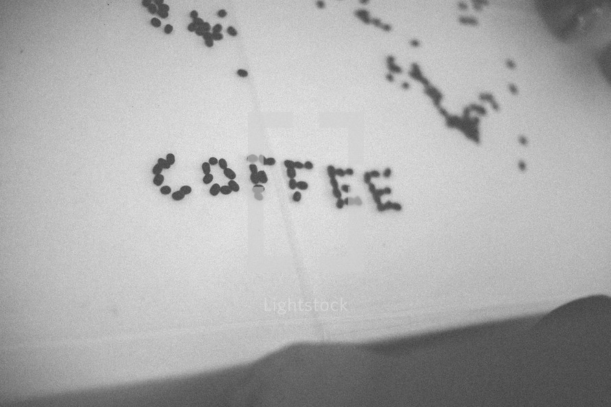 "Coffee" spelled out in coffee beans on a table covered with white linen.