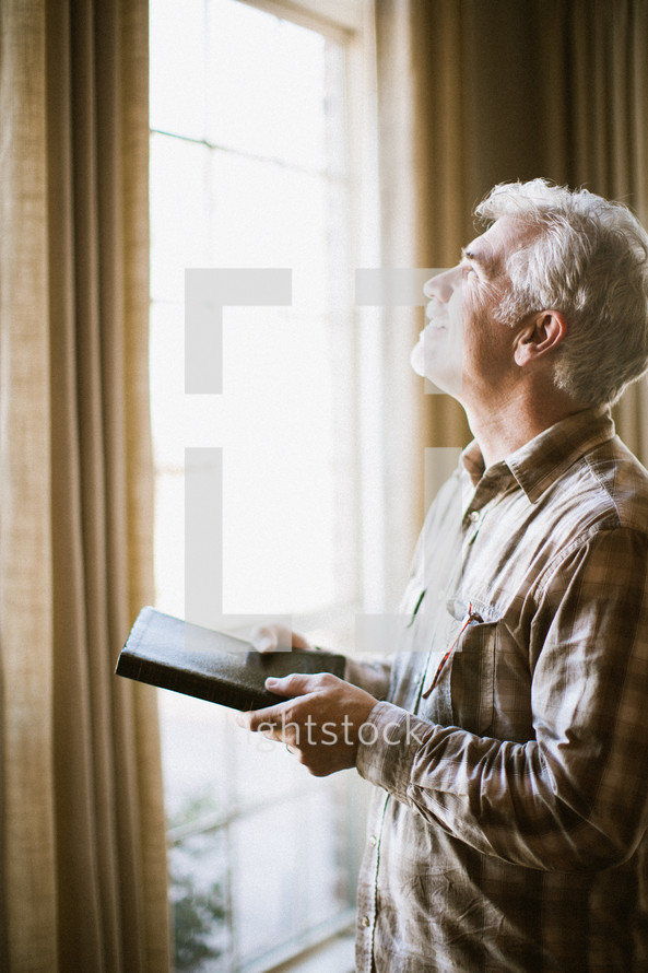 Man looking out window with Bible in his hands.