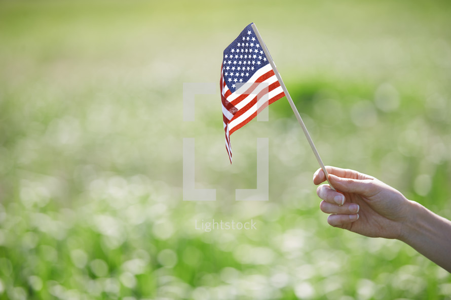 Hand of woman holding US flag in a grassland