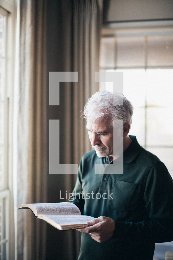 Man reading Bible in front of window.