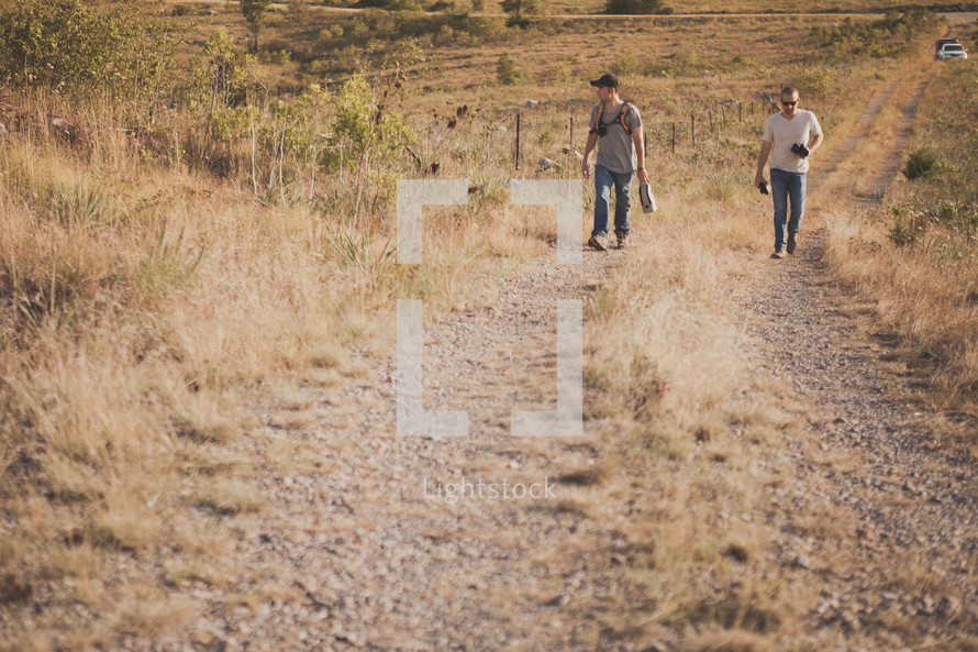 Two men walking up a hill on a dirt road.