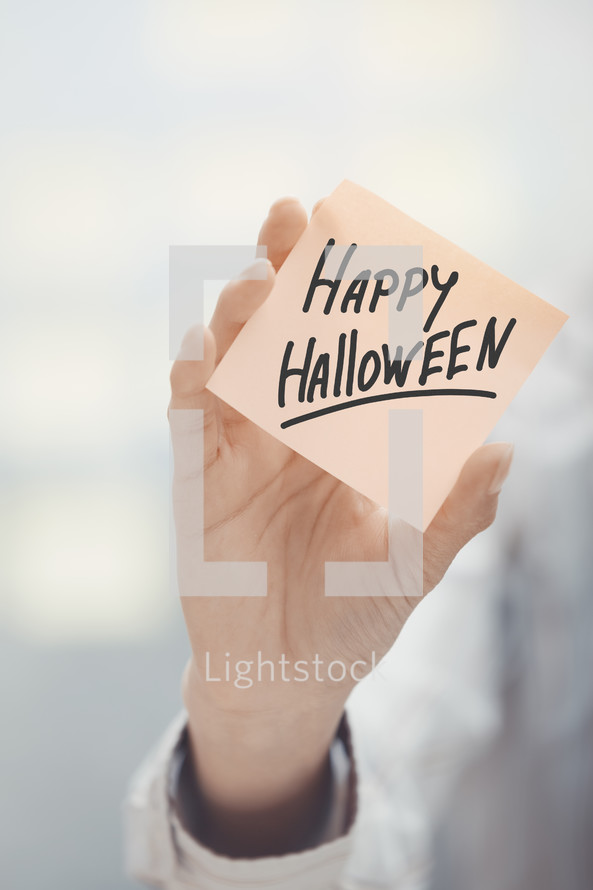 woman holding a sticky note with the words Happy Halloween 