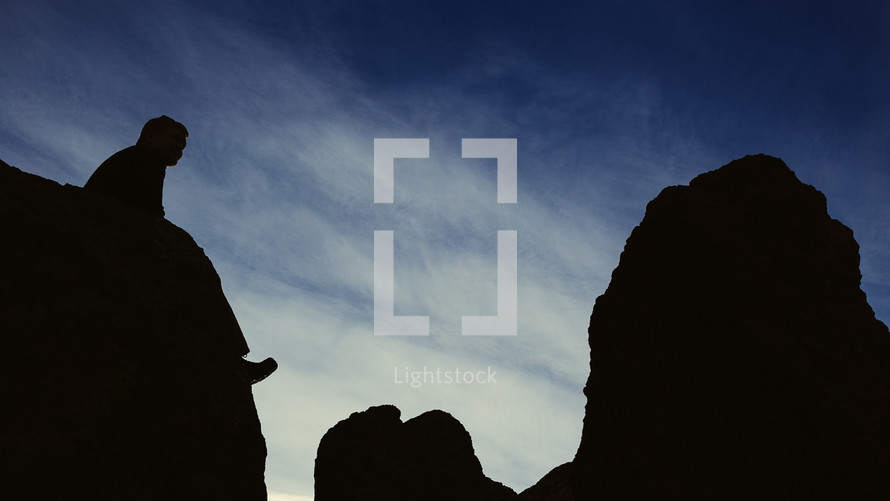 Silhouette of a man sitting on a rock formation. 
