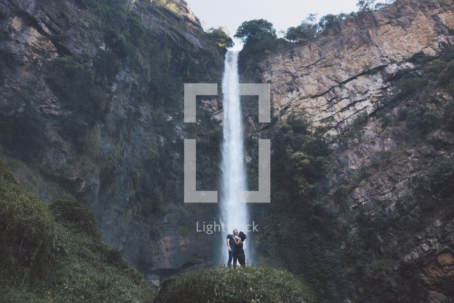 a couple kissing in front of a waterfall 