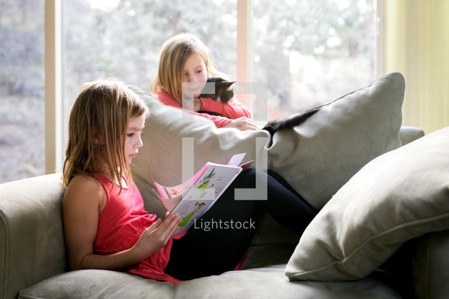 sister's reading a children's book together on a couch 