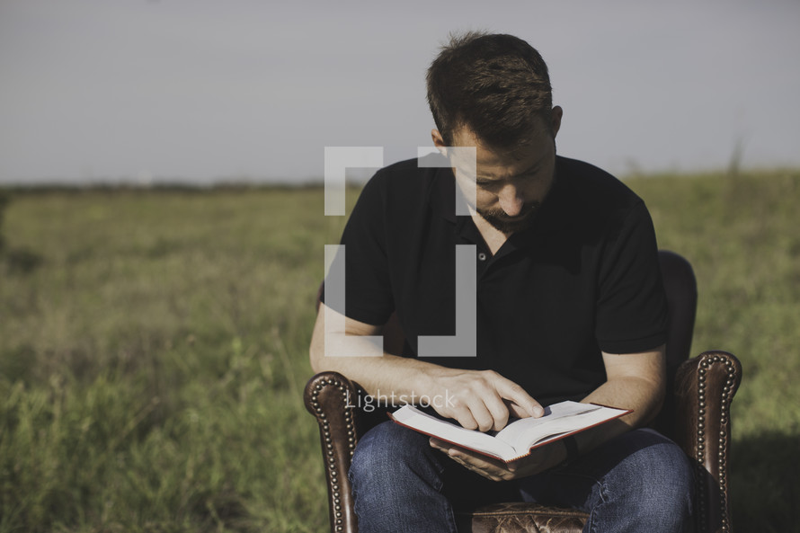 a man reading a Bible in a leather chair in a field 