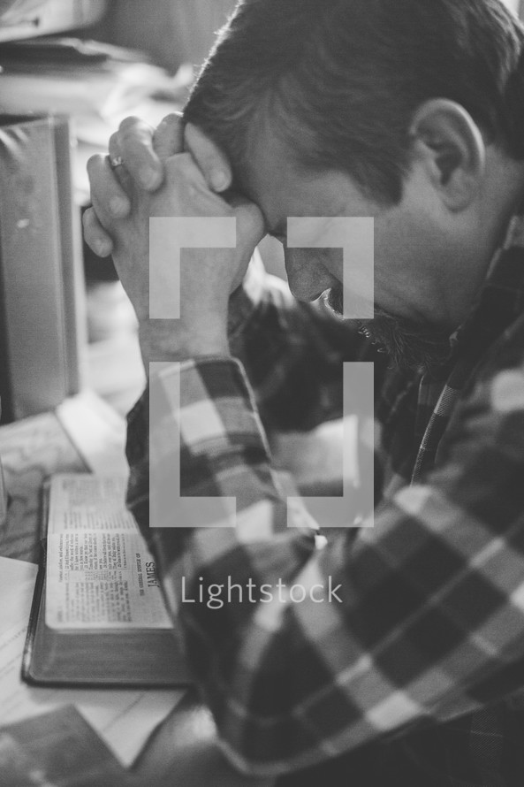 a man sitting at his desk praying and reading a Bible 