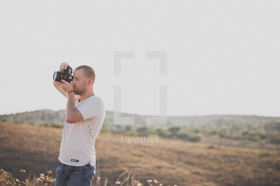 Man with a camera standing in a field taking pictures.