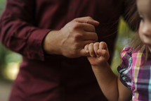 a toddler girl hanging onto dad's finger 