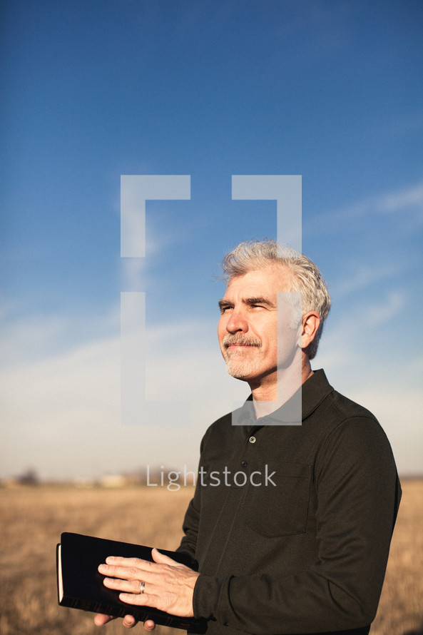 elderly man standing in a field with his hand on a Bible