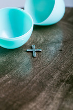 Silver cross on a wooden table with a plastic Easter egg.