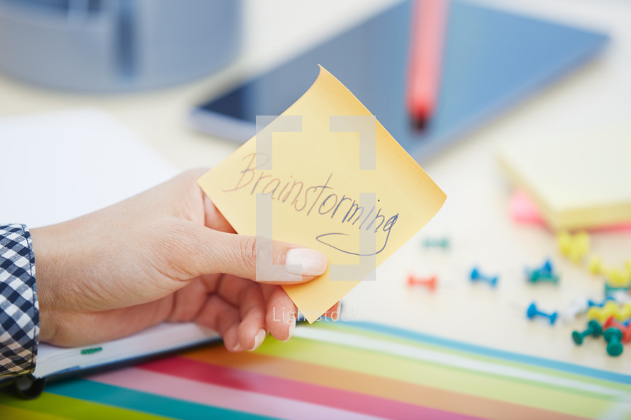 a woman holding a sticky note with the words brainstorming 