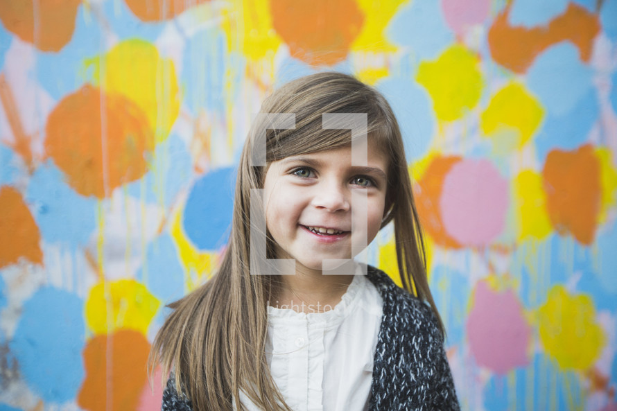 a young girl standing in front of a colorful wall 