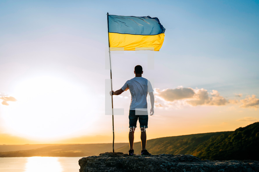 Happy ukrainian man with national flag on summer sky background on high rock. Patriot symbol. Free Ukraine. High quality photo