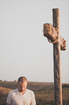 Man with head bowed at a wooden cross on a hill.