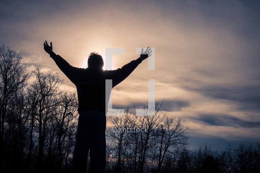 Man with arms outstretched in praise during sunset 